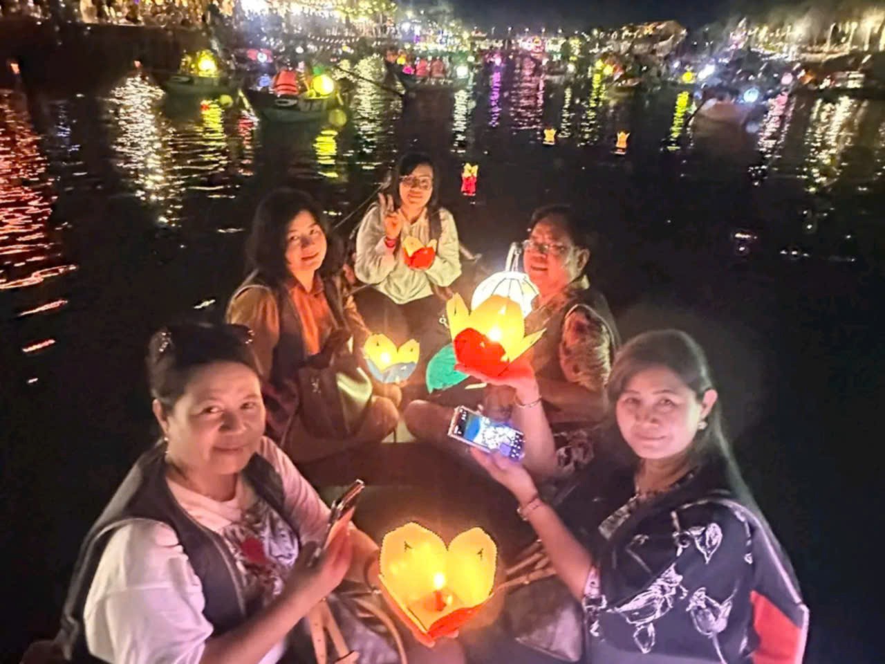 Group of women taking photos with candle lights during a lantern boat ride in Hoi An at night