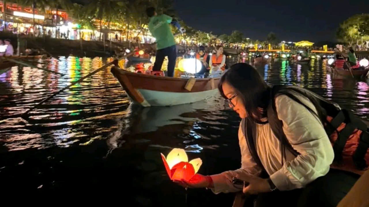 Woman releasing a floating lantern during a lantern boat ride on the Hoai River in Hoi An at night